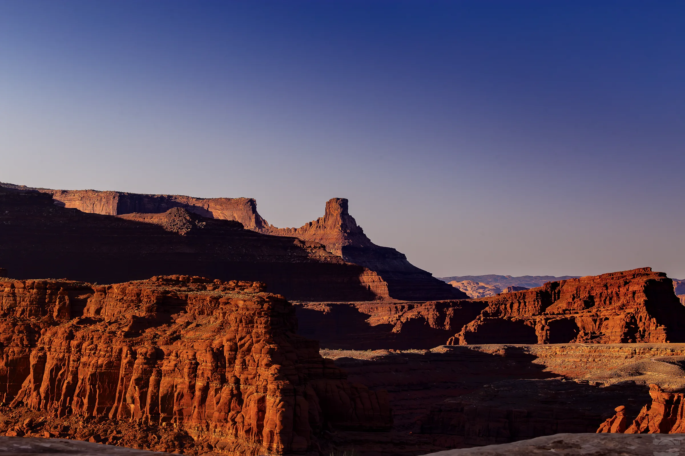 Red sandstone cliffs and a narrow rock tower under a gradient blue sky.